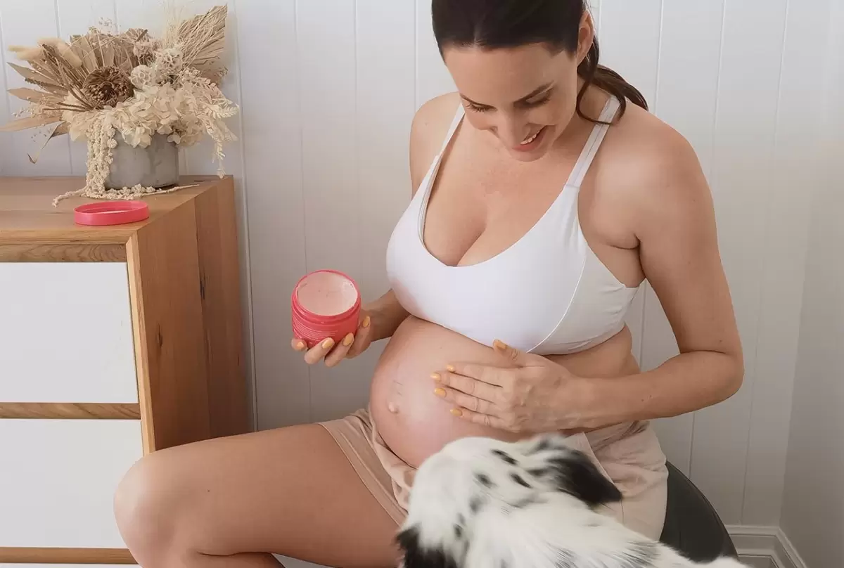 Mum applying cream to her baby bump to soothe a pregnancy skin condition.