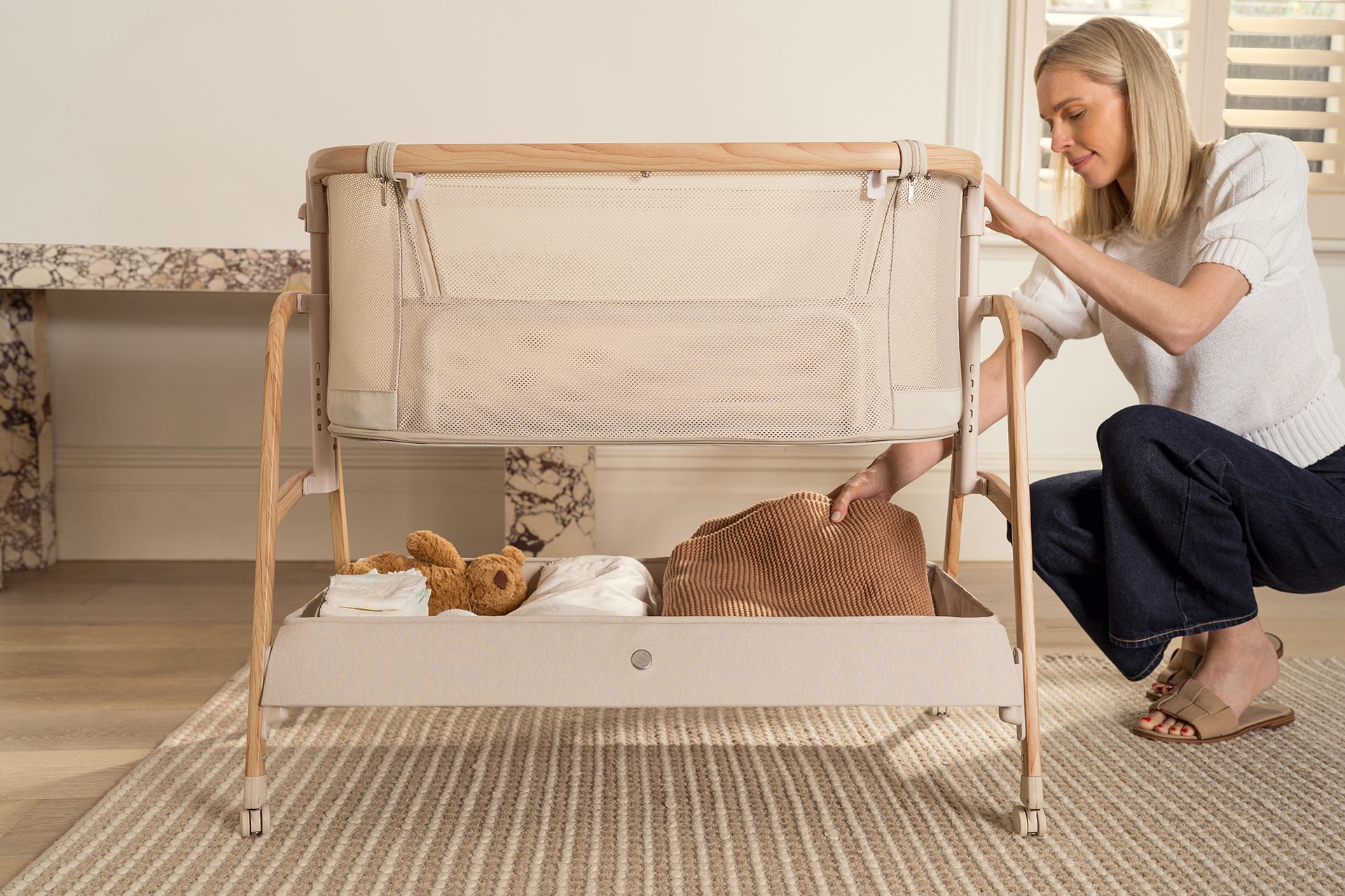 Mum seated while organising clothes, a baby blanket and essentials in the Babybee Pod storage section, a feature that helps the best baby bassinet keep everything within easy reach.
