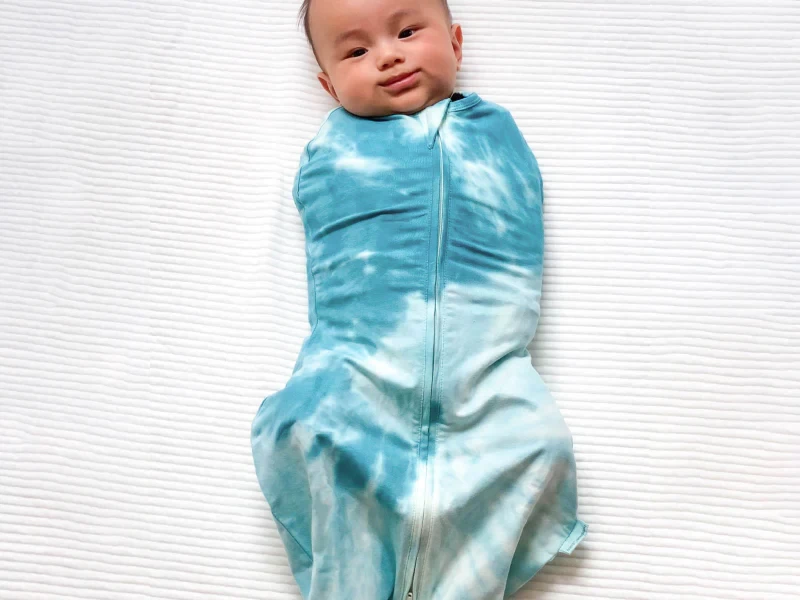A baby in a tie dye happiest baby sleepea swaddle