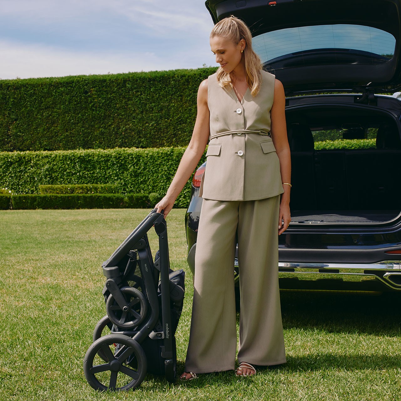 Mum standing at the back of a car holding a folded pram ready to place in the open boot, showing the compact fold of the best double pram.