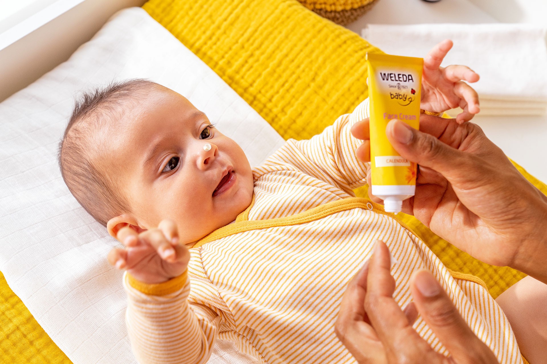 Baby in romper lying on changing station while mum applies gentle Weleda cream – showcasing the best baby skincare care moment.