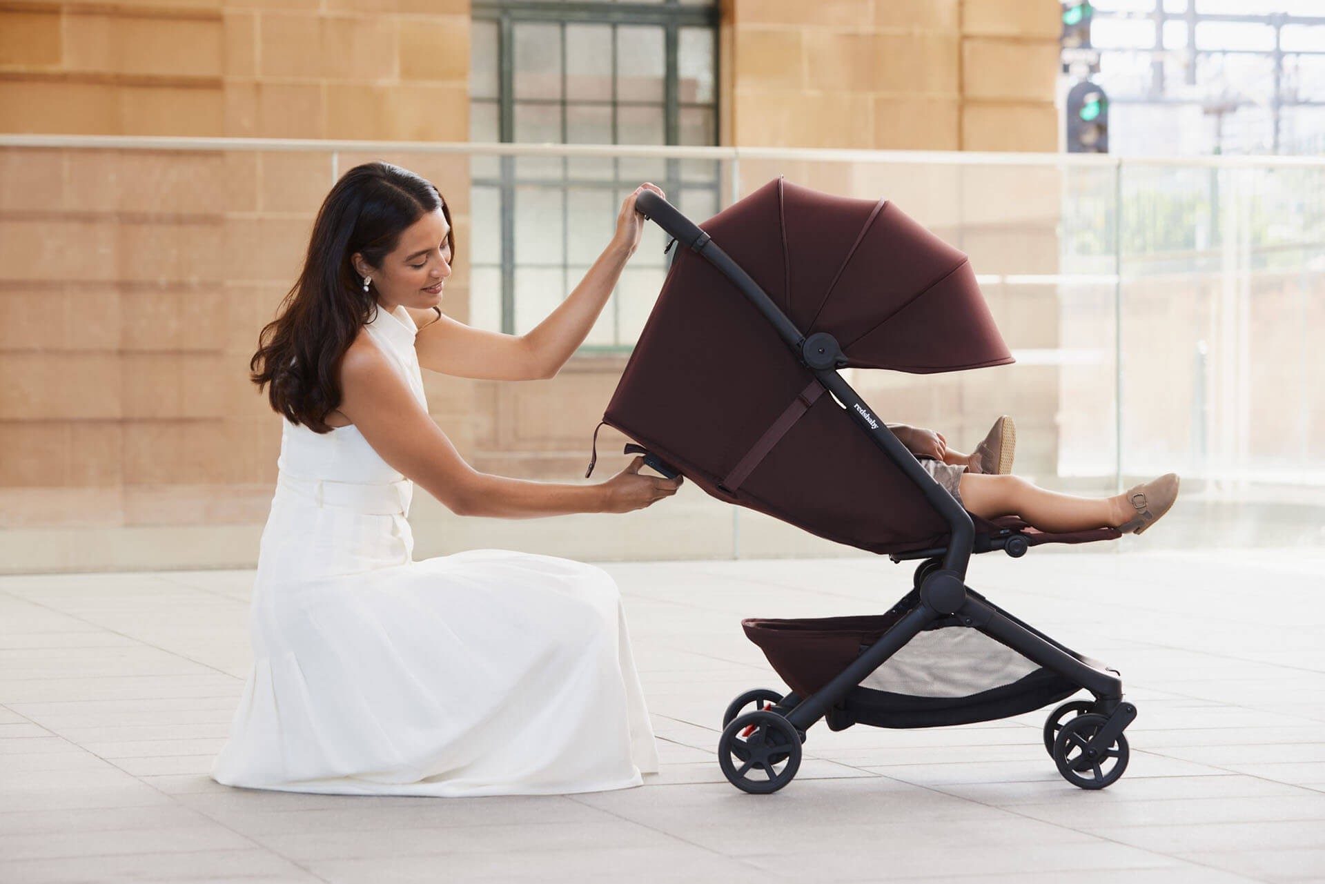Close-up of a mother setting up the maroon Redsbaby SKIP³ Travel Pram for her child.