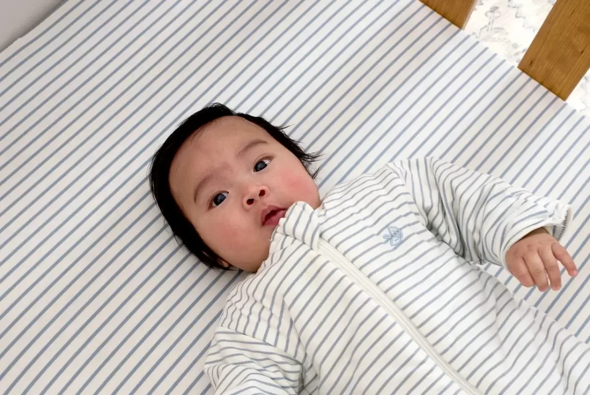 a baby lying on striped cot sheets, a baby registry essential