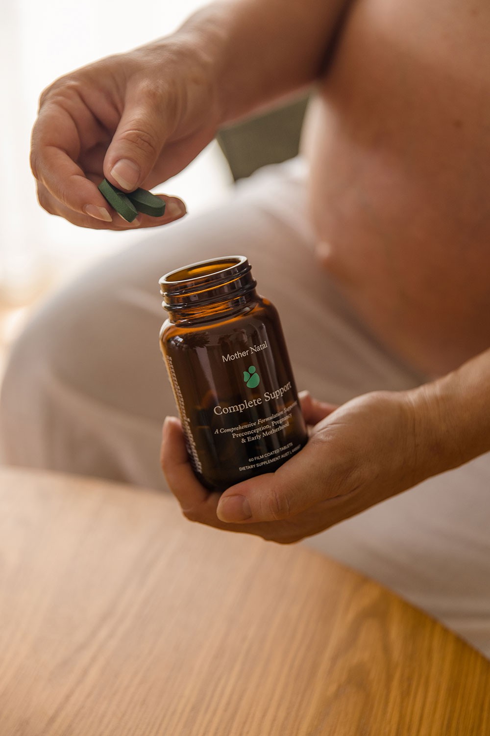 Close-up of pregnant woman holding two tablets from a Mother Natal prenatal vitamin bottle in Australia