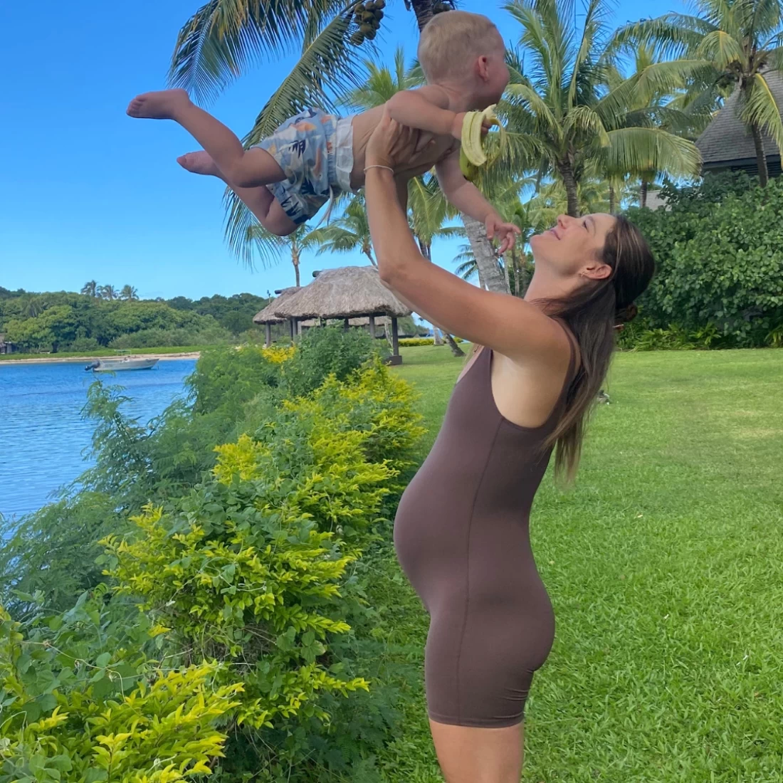 Pregnant woman lifting her child near the lake, dressed in Estroni Tank Bodysuit best maternity activewear.