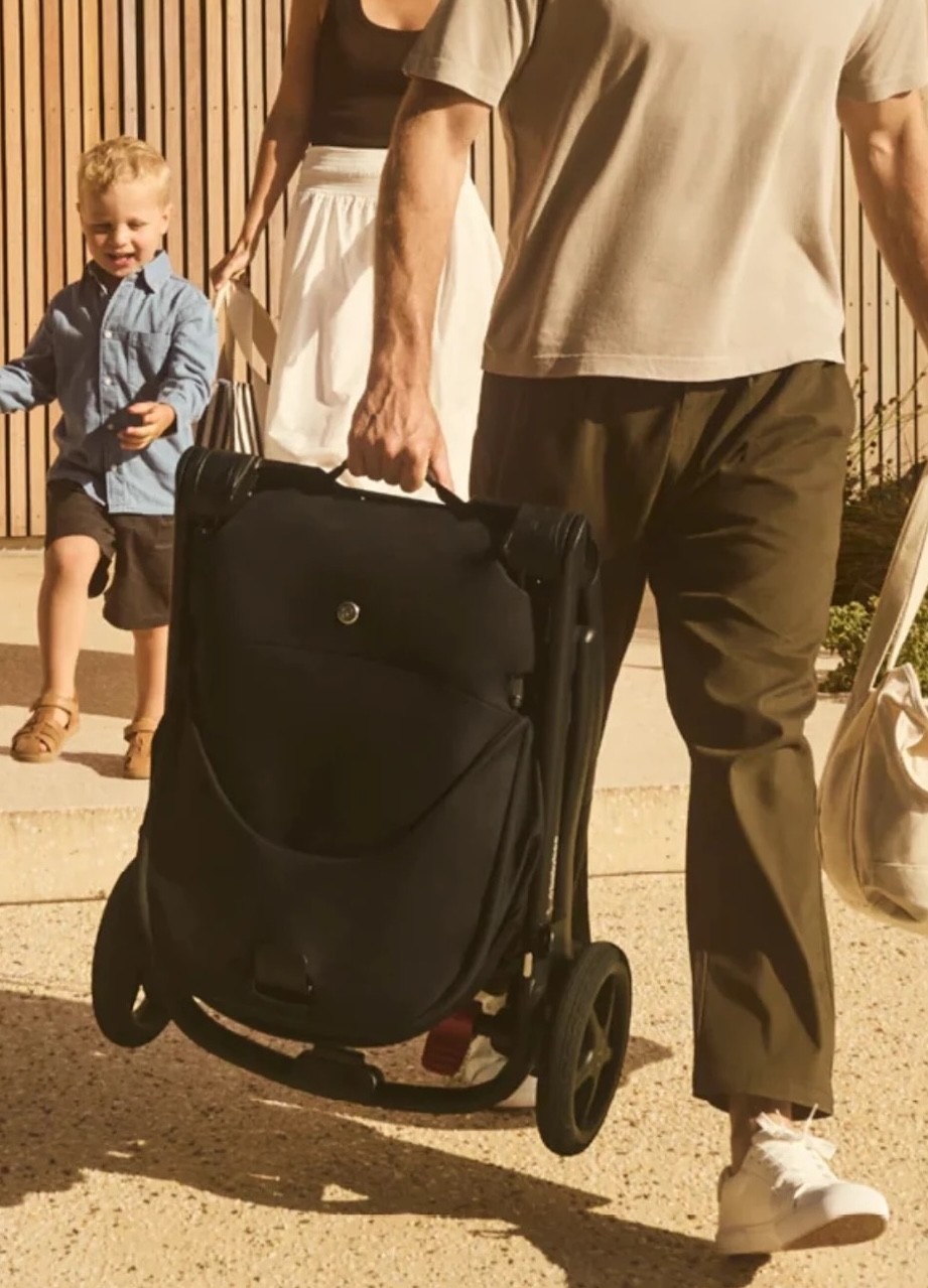 A dad carrying the Babybee Alto pram folded down