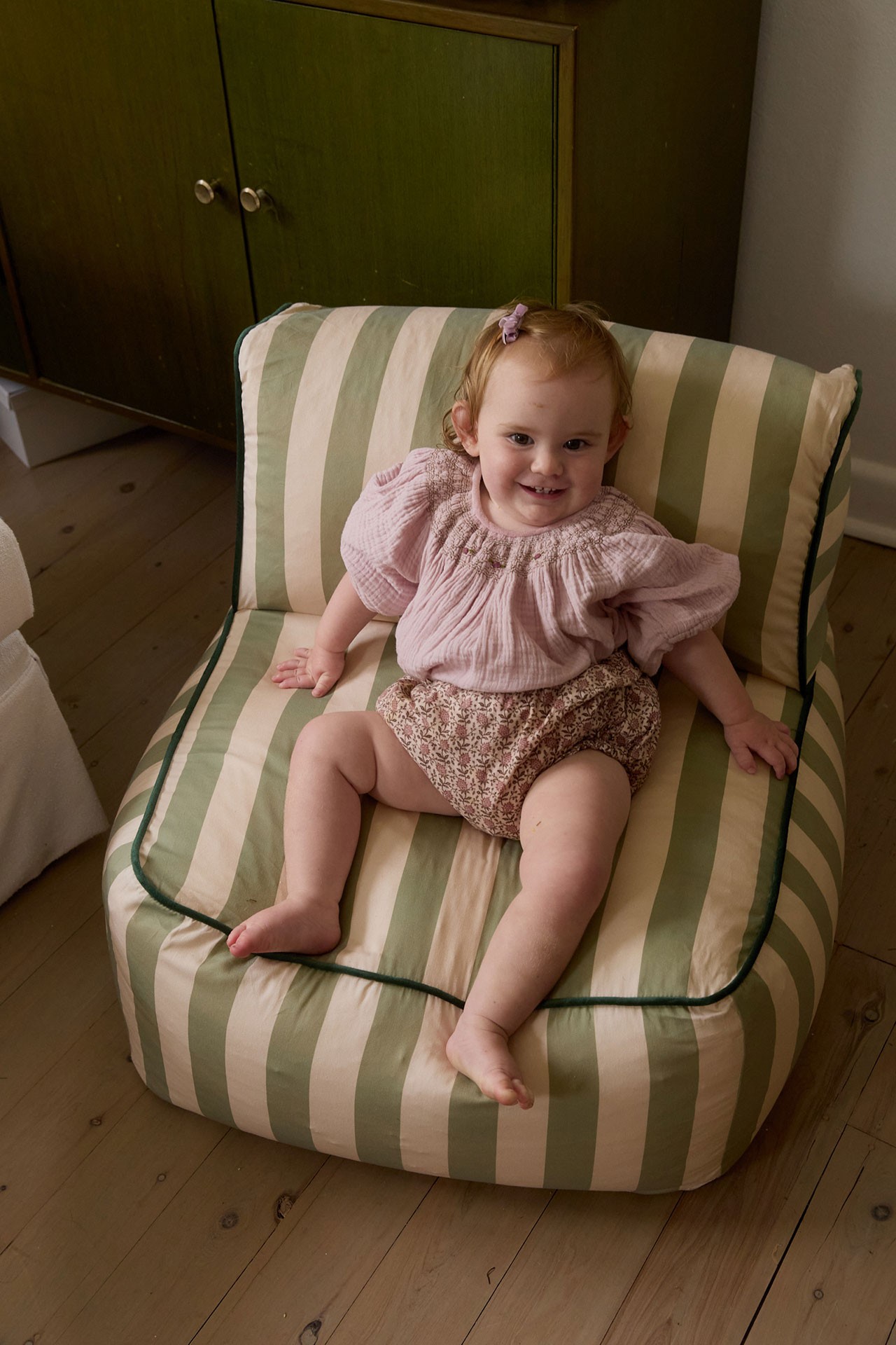 Modern children chair with wide, deep seat placed in a nursery, toddler girl seated happily for play or relaxation.