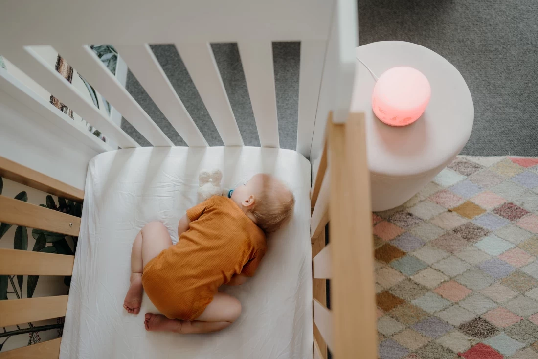 Sleeping baby next to Glow Dreaming Glow Sleep Easy best white noise machine on table beside the crib.