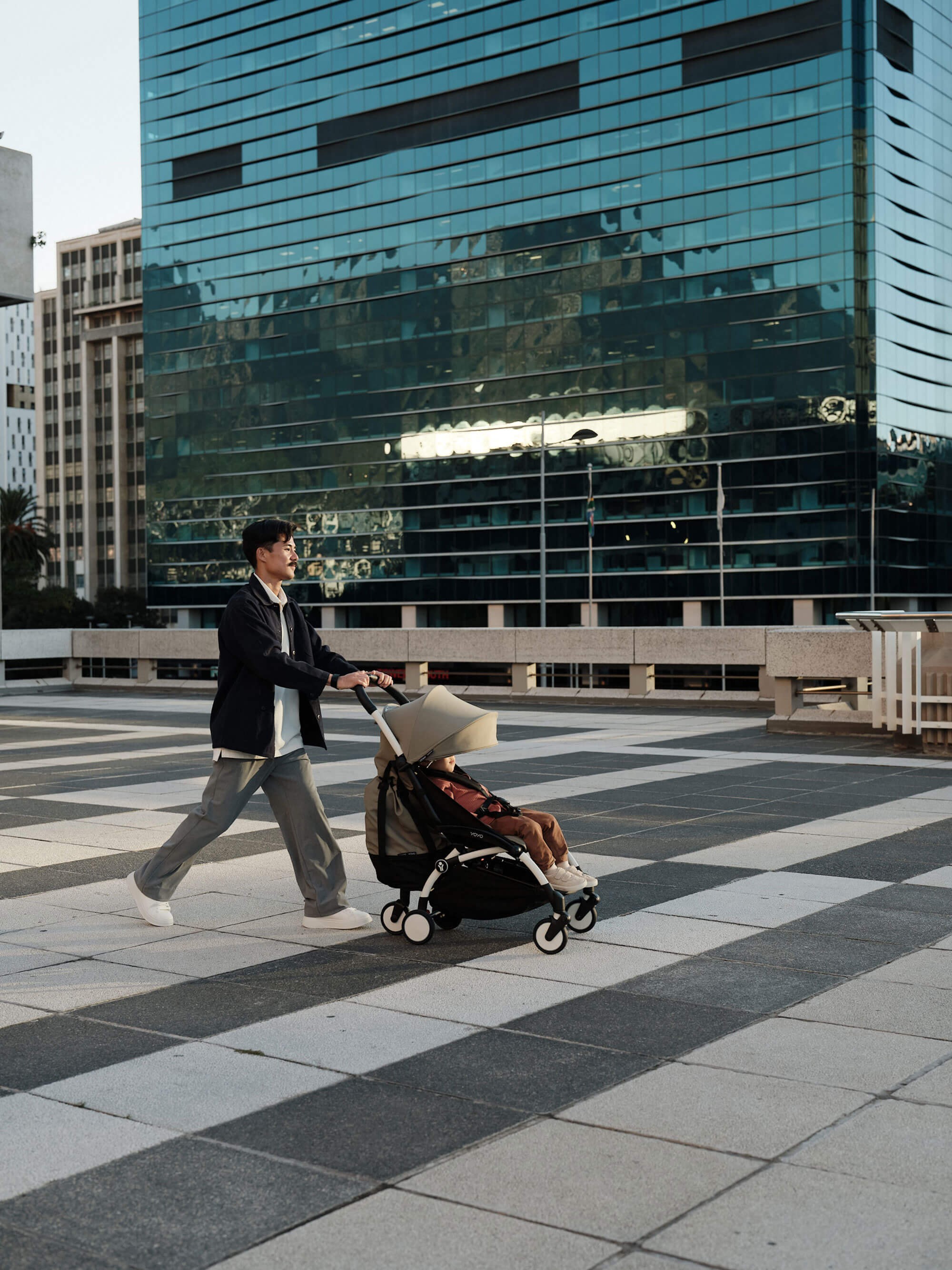 Dad walking outdoors while pushing the Stokke Yoyo³ Travel Pram with his child.