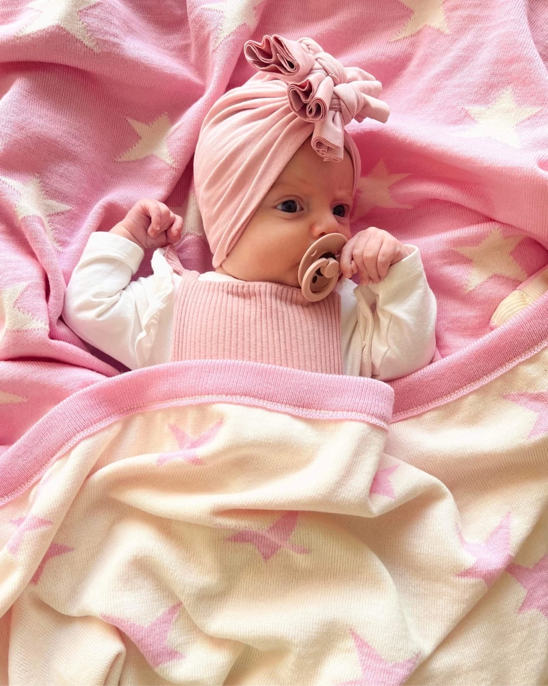Newborn resting on the best baby blanket in soft pink merino wool.