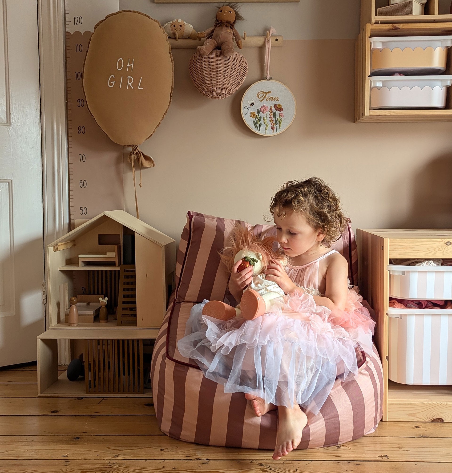 Young girl in a fairy dress playing with a plush toy while seated on the best children's chairs in pink stripe cover inside a nursery playroom