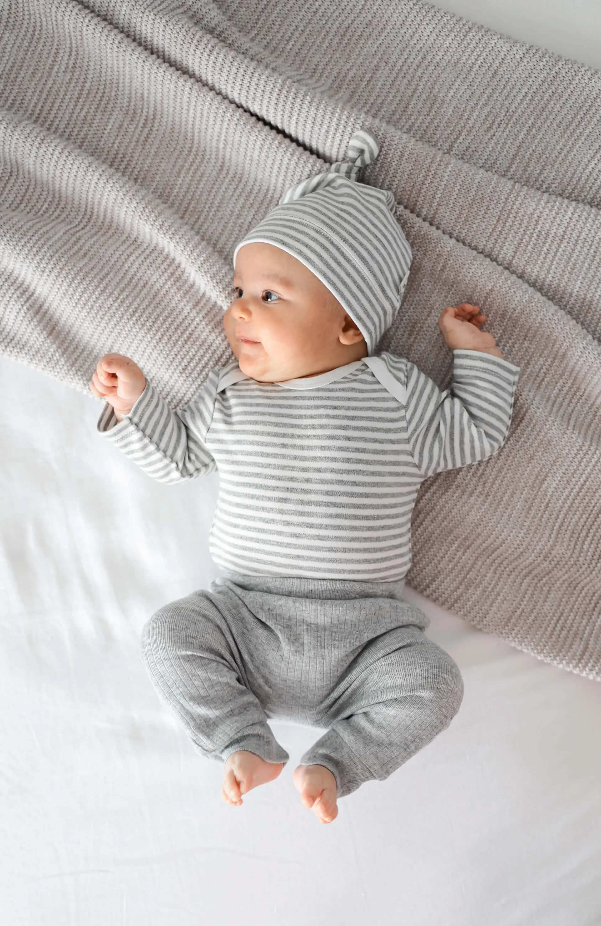 Smiling baby dressed in vibrant Lummi In Colour Babywear lying on soft bed, representing best baby clothes designed for comfort