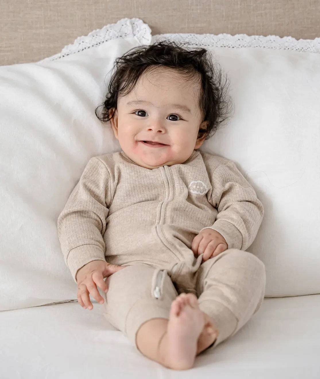 Happy baby photo of infant smiling while lying on bed in Lummi In Colour Babywear, one of the best baby clothes in Australia.