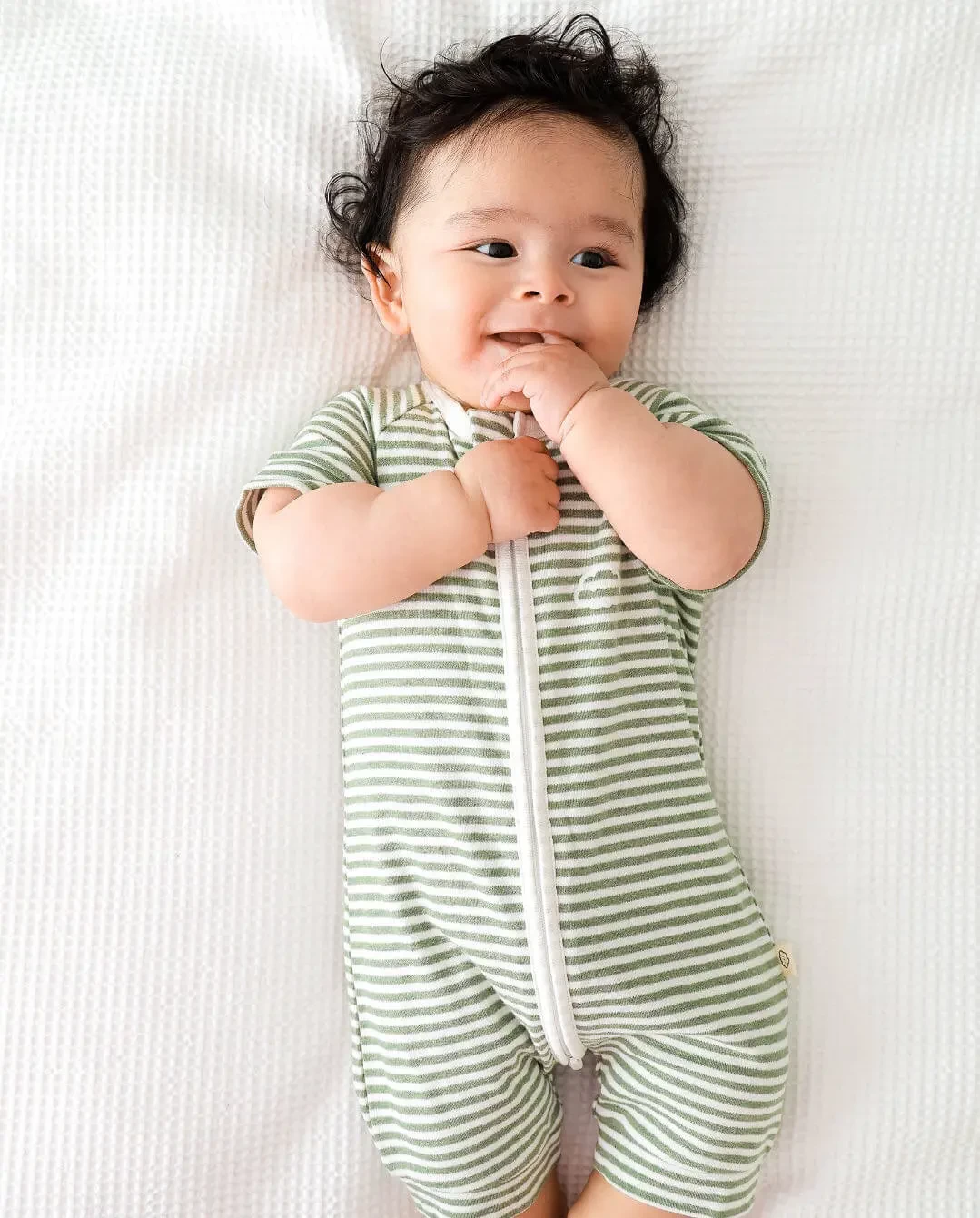 Lying baby dressed in Lummi In Colour Babywear on soft bed, representing best baby clothes designed for everyday comfort