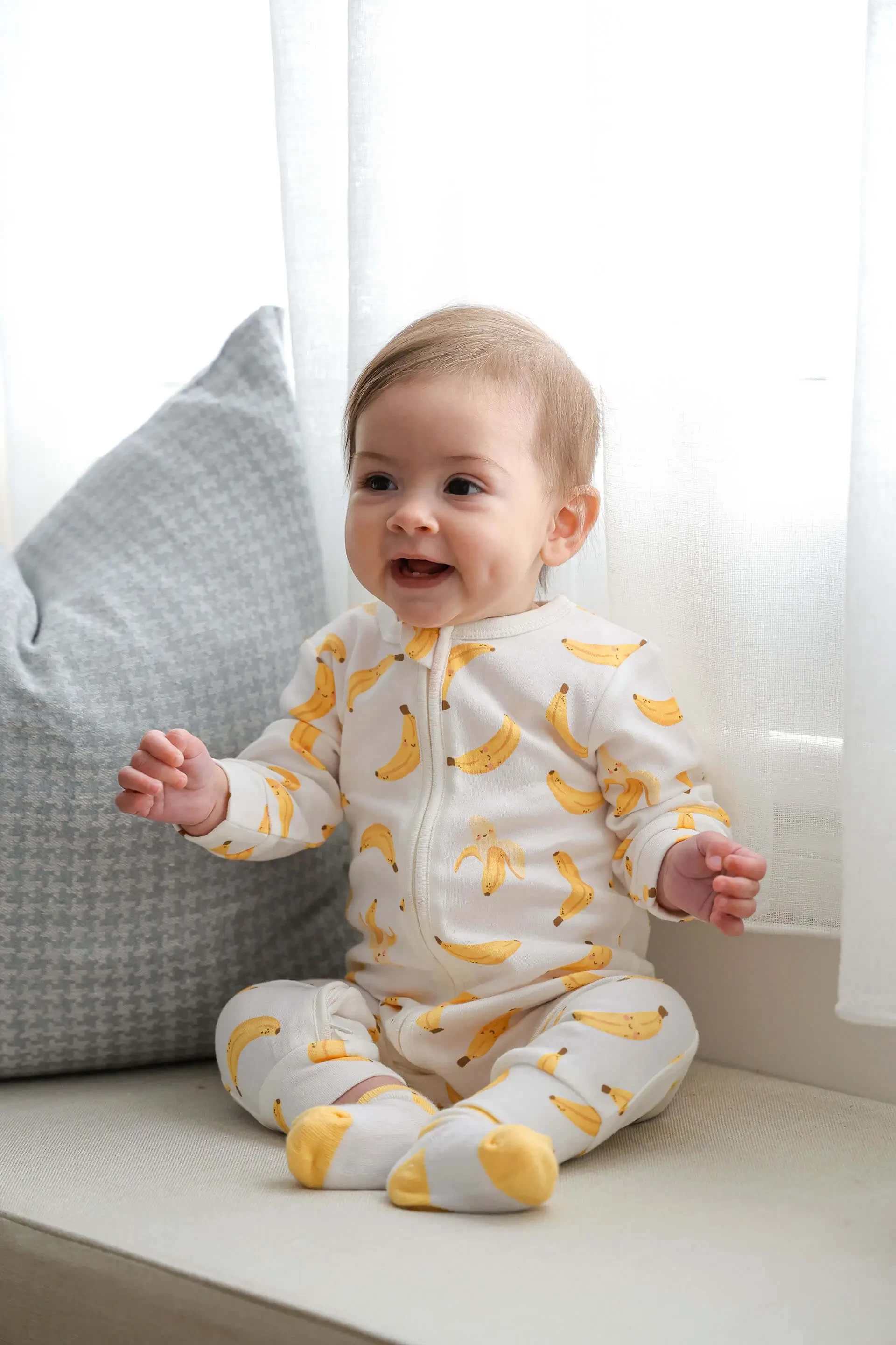 Adorable baby in Lummi In Colour banana print babywear sitting comfortably on a couch, representing best baby clothes in Australia