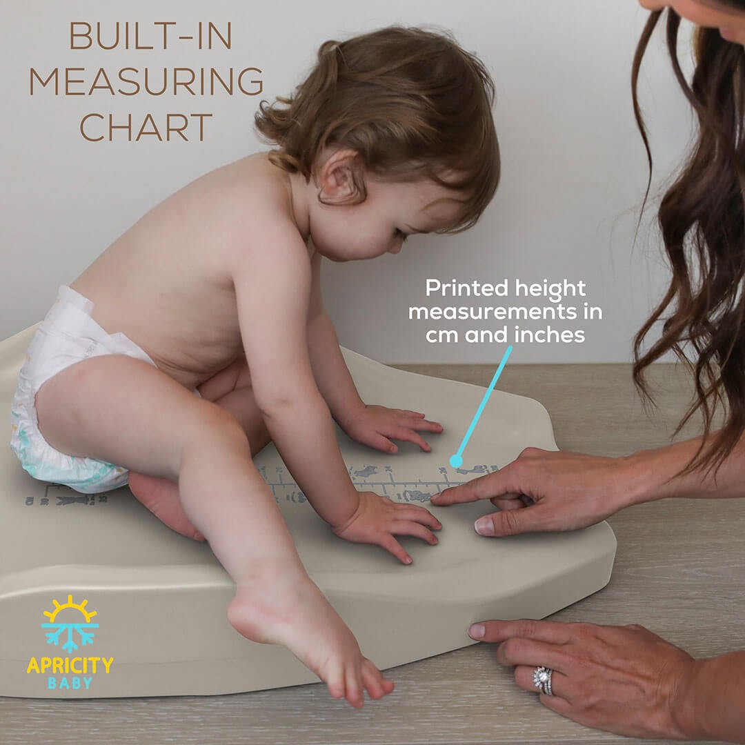 a baby sitting on a changing pad for newborn with a built in measuring chart being pointed by a mother