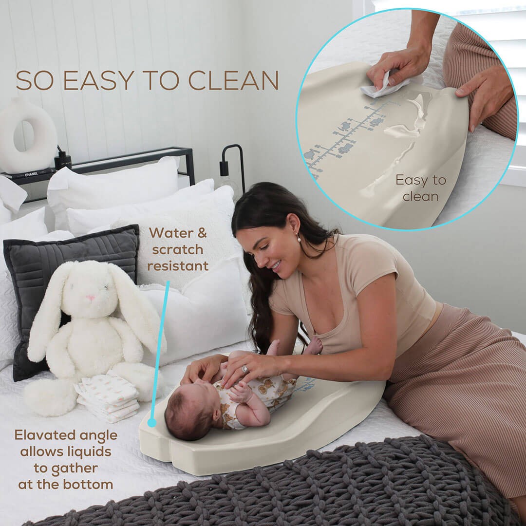 A mother seated on the bed while changing her baby nappy lying on the best changing pad from Apricity