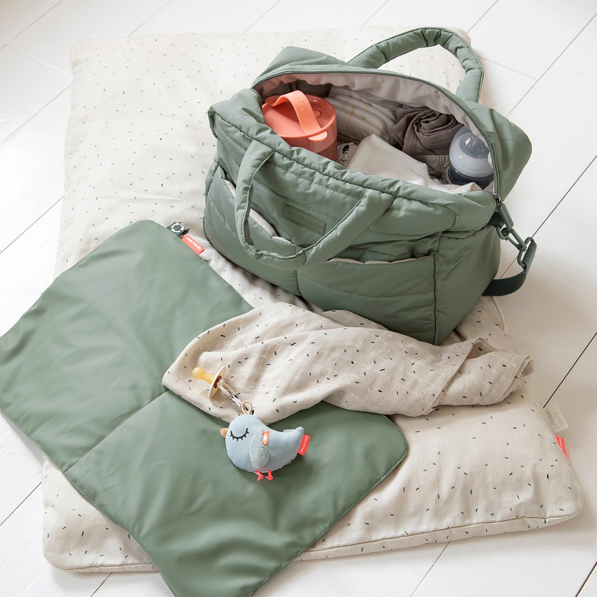Done by Deer nappy bag in green filled with baby essentials, paired with matching padded change mat laid out on the floor