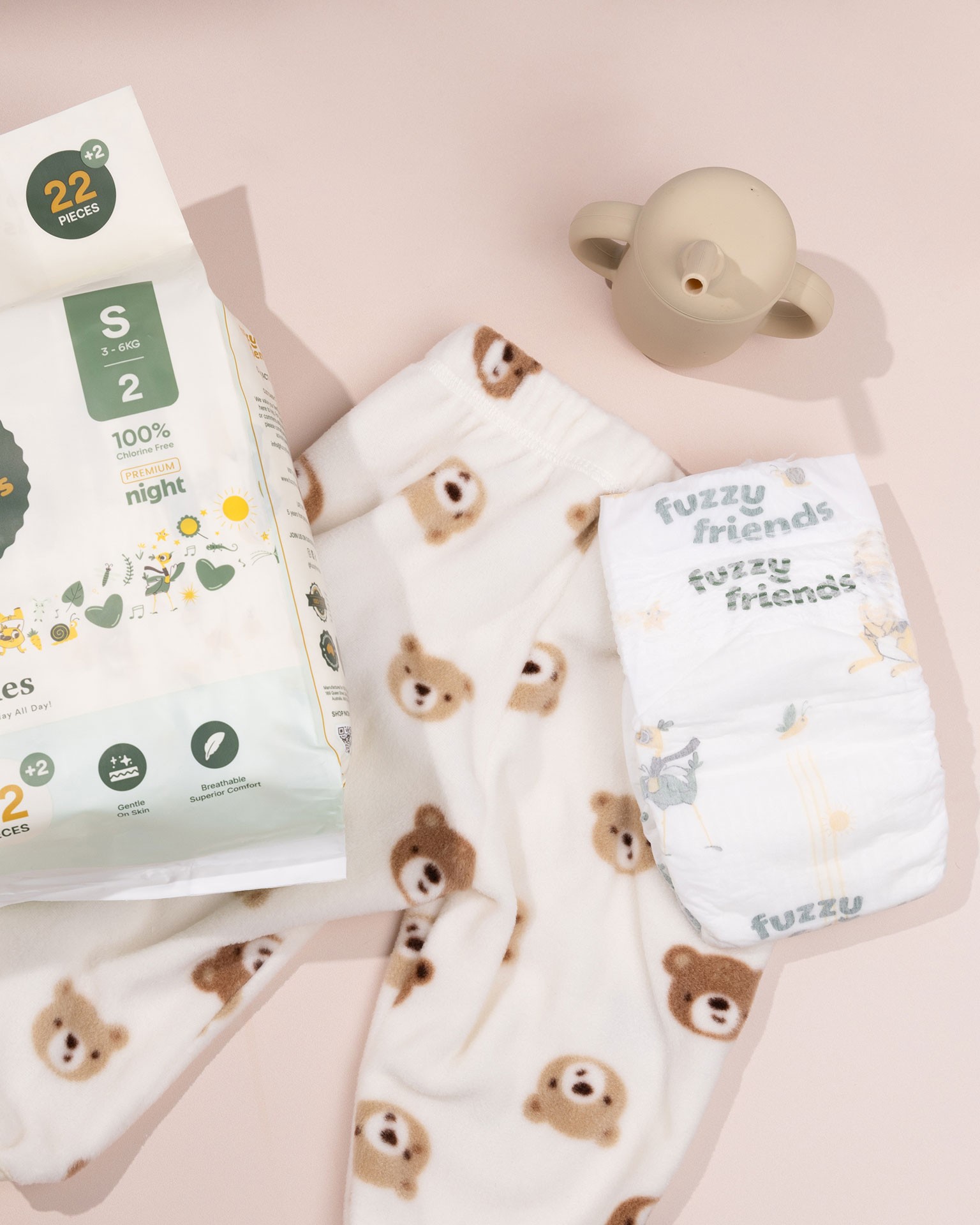 A pack of Fuzzy Friends disposable nappies - best baby nappy brand, a baby bear pyjama and sippy cup flat lay