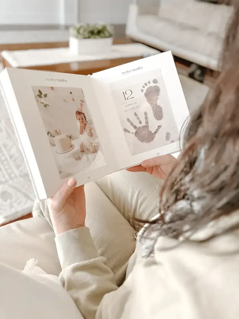 A woman holding a baby milestone book with baby photos and inkless baby footprint & handprint
