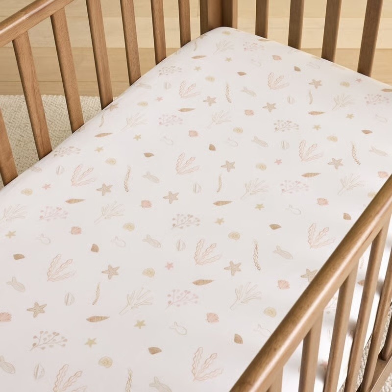 A baby cot shown with cot sheets covered in seashells
