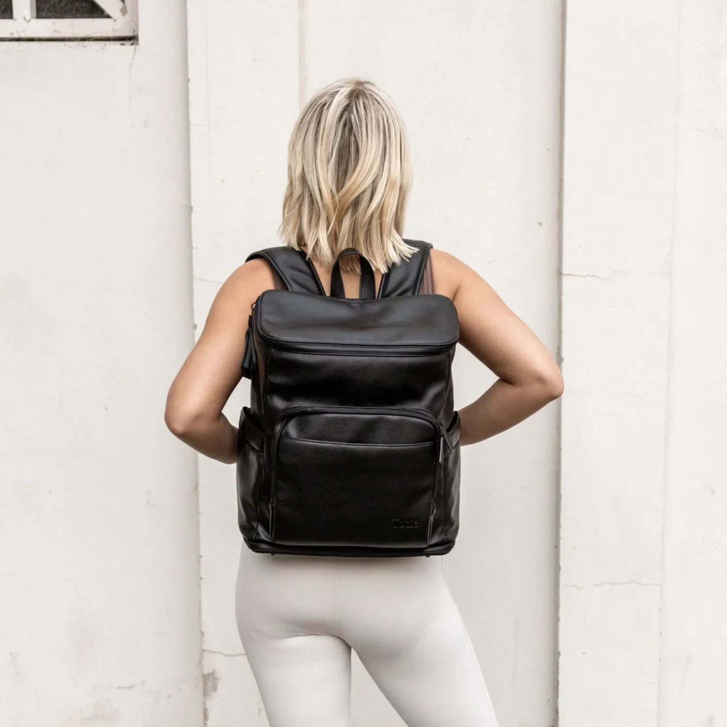 A woman with blonde hair wearing the Tottie backpack, shown from behind