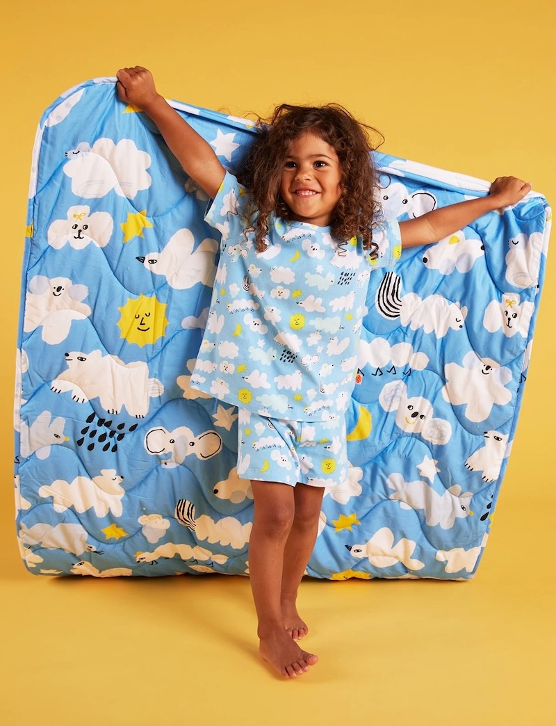 A little girl holding up a Halcyon Nights cot quilt in fun cloud print
