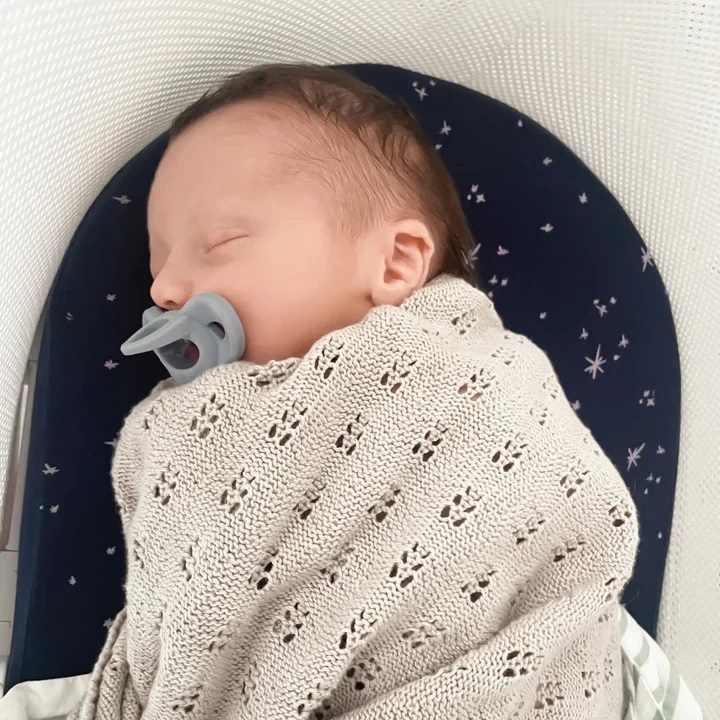 A baby lying in a bassinet in a swaddle with the Minbie dummy