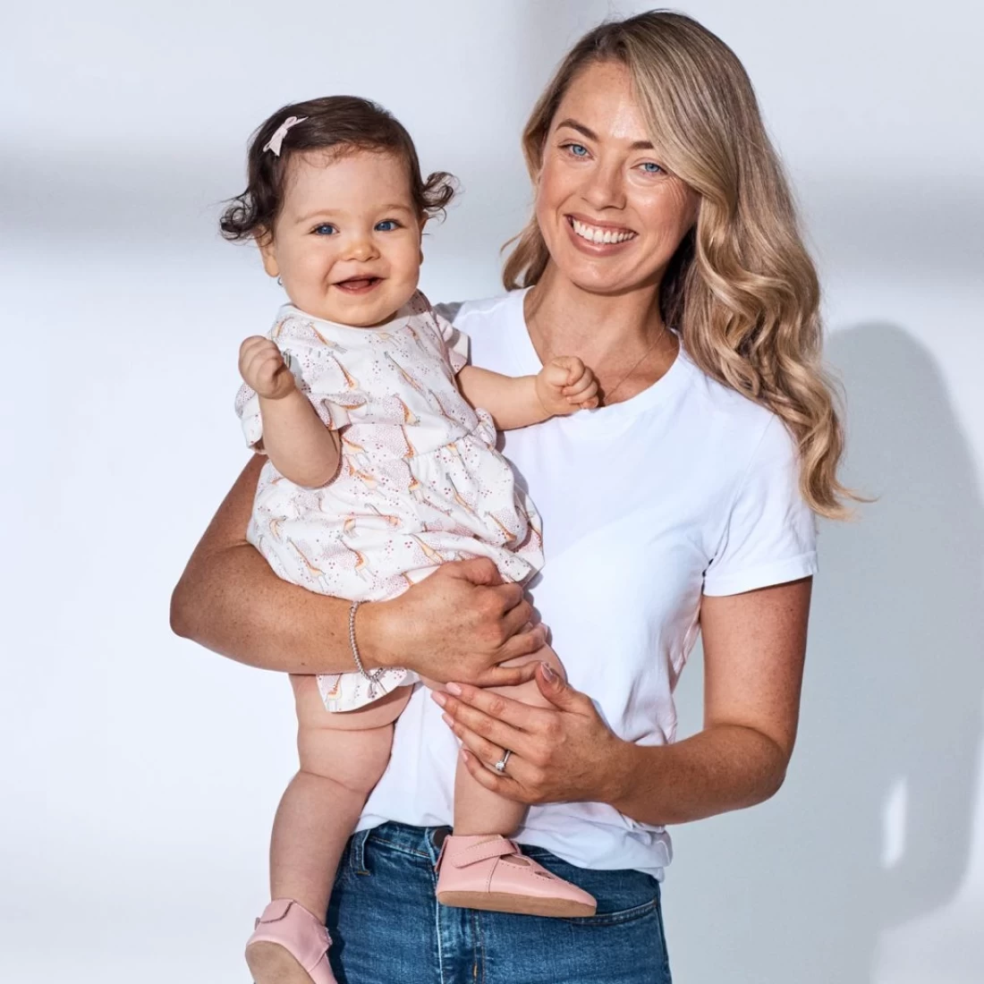 Mum carrying her baby dressed in a cute romper – one of the best baby items for gift registry.