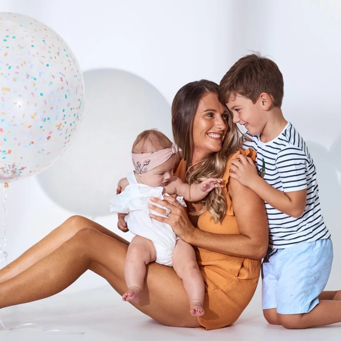 Mother sitting with her kids dressed in quality baby clothes, highlighting the best baby items for gift registry