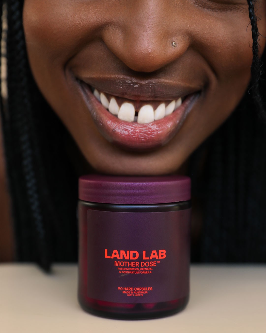 Woman smiling brightly with her chin resting on a bottle of Land Lab Mother Dose prenatal vitamin.