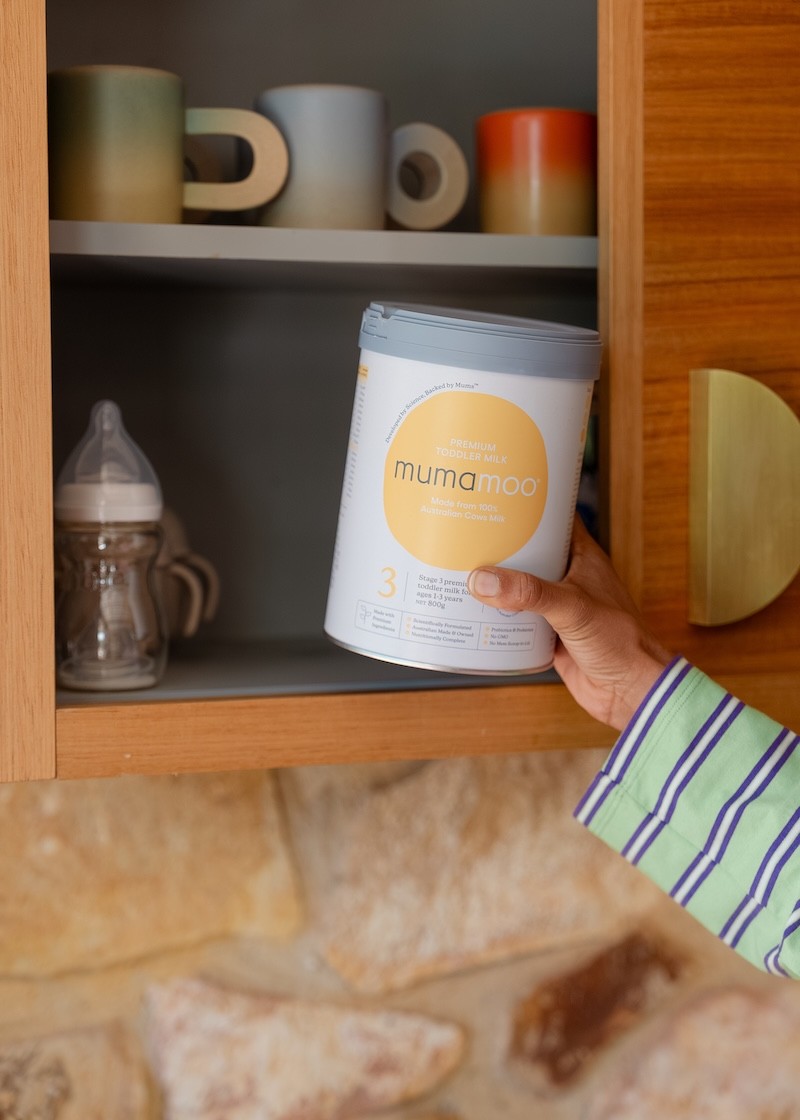 A can of toddler milk being taken off the shelf by a child