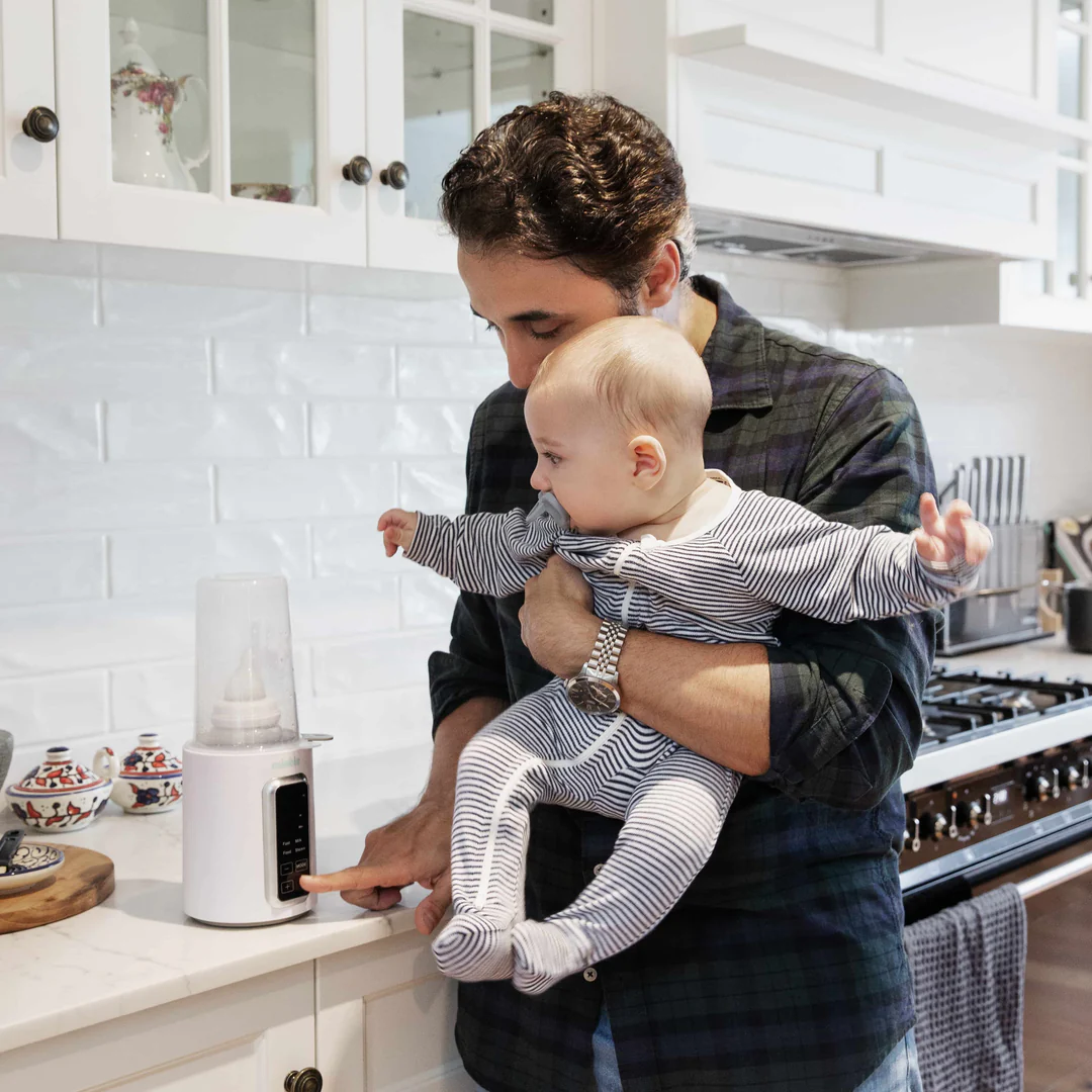 Dad holding baby while using Minbie bottle warmer for feeding