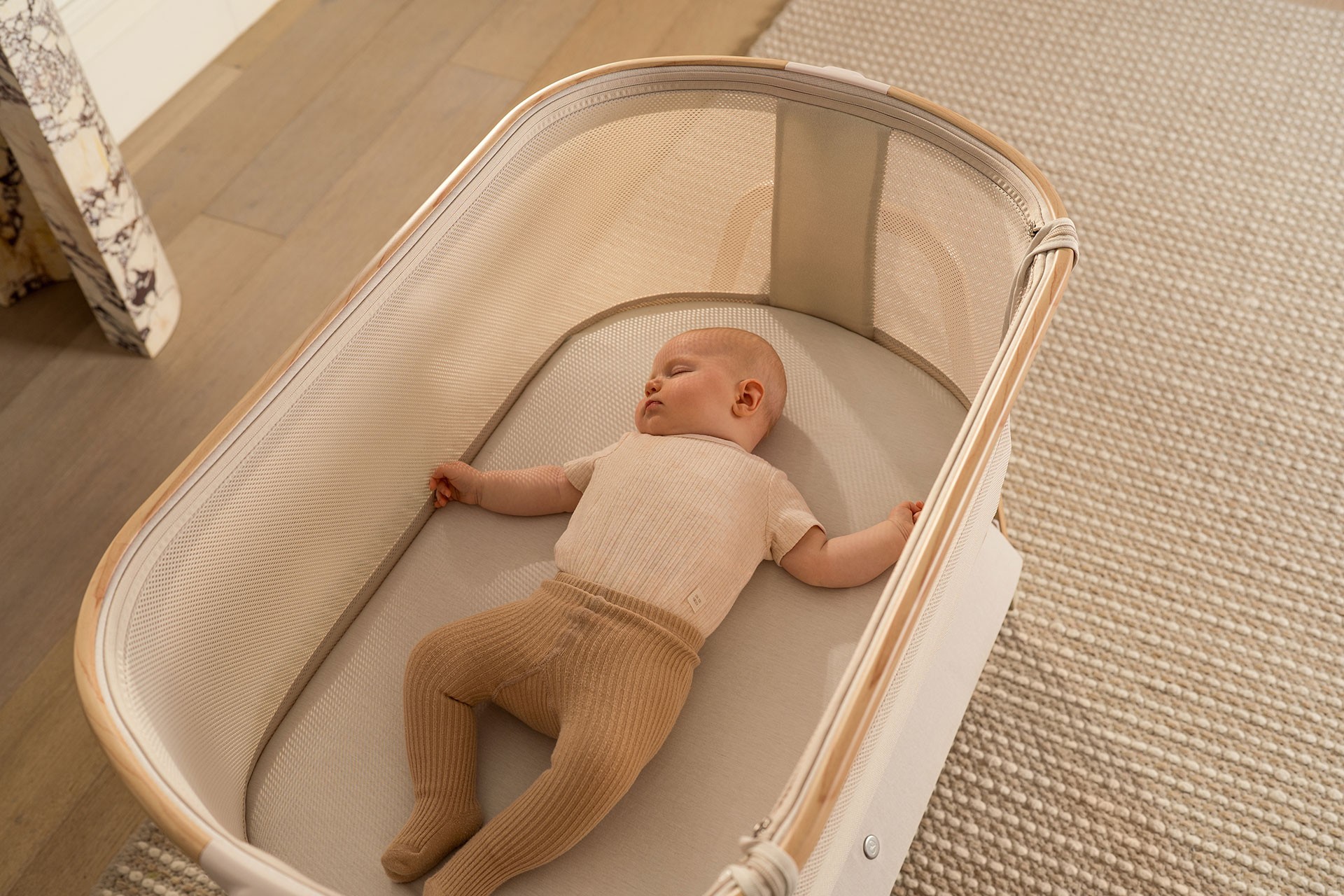 Infant sleeping inside a wooden and mesh bassinet in the nursery room, showing the supportive and breathable style often chosen as the best infant bassinet