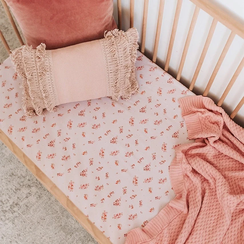 A pink baby girl cot set up with floral cot sheets