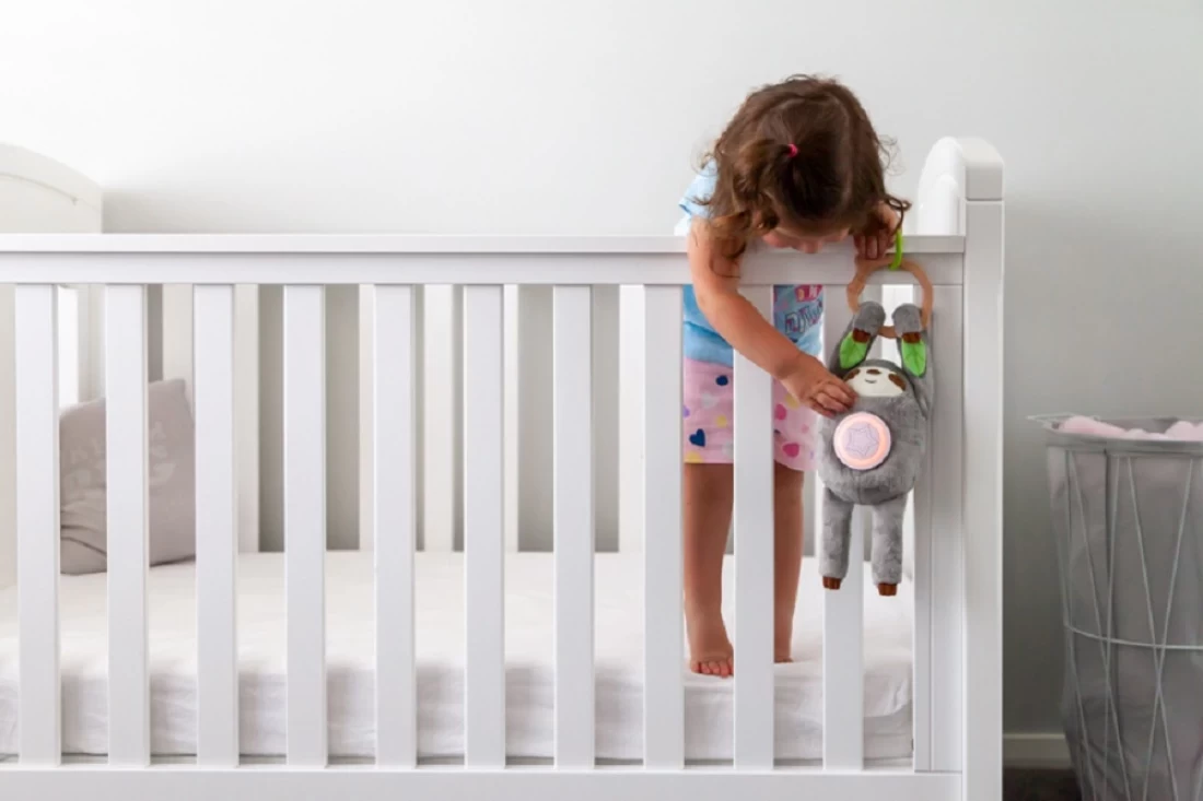 lose-up of toddler on crib grabbing Santi the Sloth sleep aid
