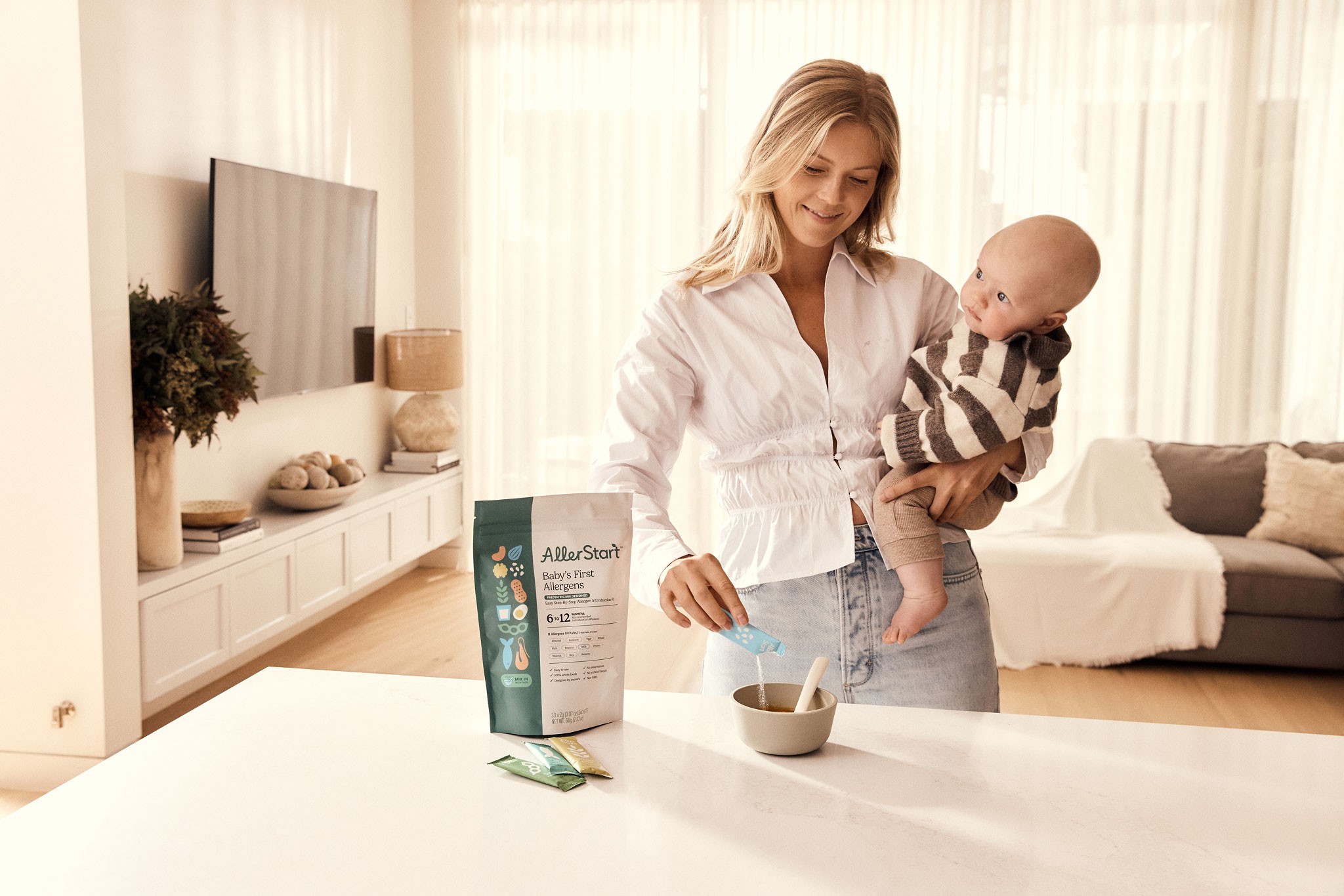 A mum preparing organic baby food at the kitchen countertop while holding her baby on the other arm