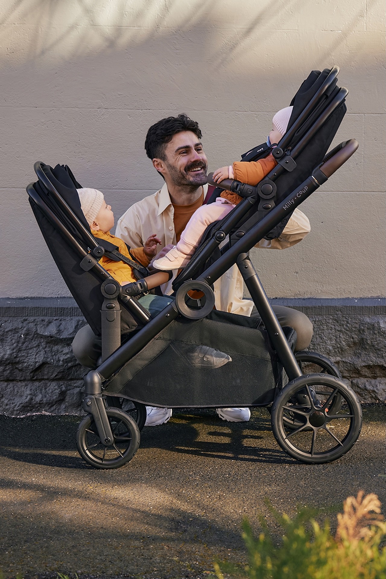 A dad talking to his two children seated in the Milly + Coup Leo affordable double pram