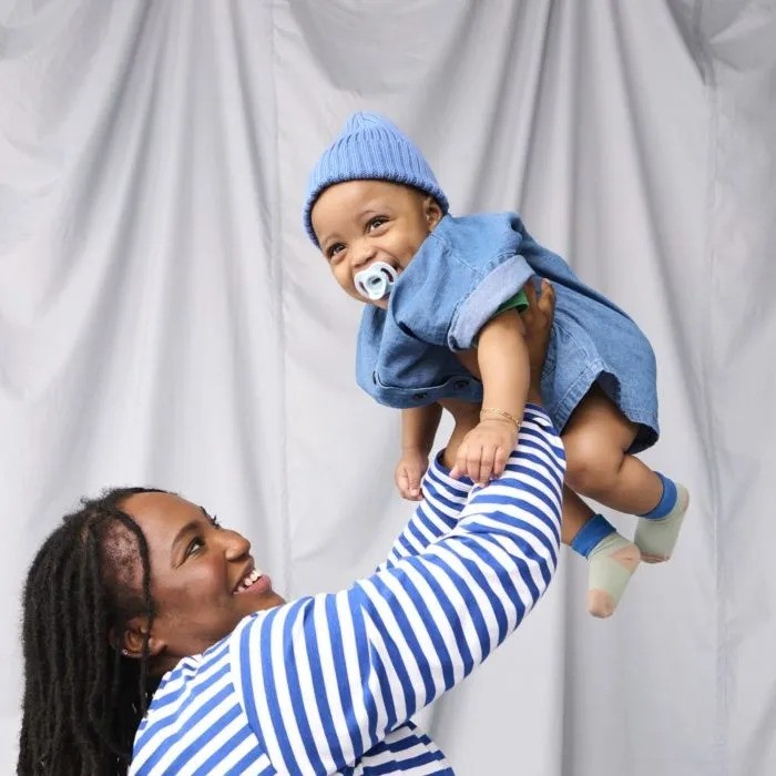 A mum holding her baby in the air, the baby using a Tommee Tippee dummy