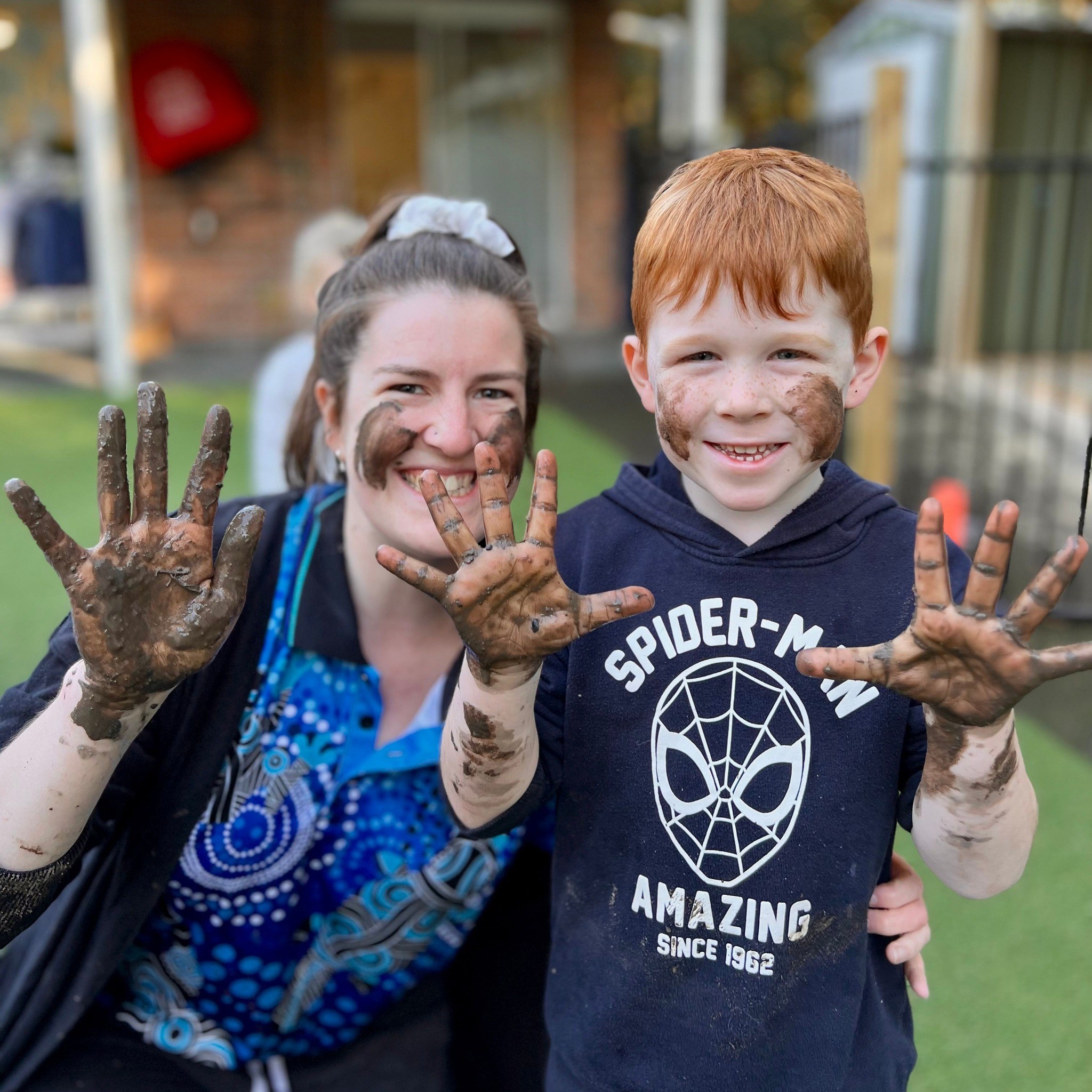 Educator and toddler proudly showing their dirty hands after play at the best childcare and daycare centre