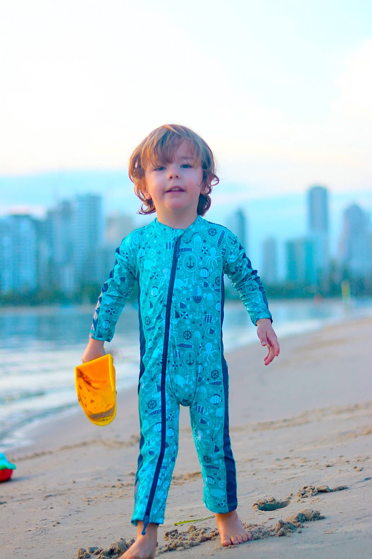 Printed dark blue full coverage swimwear worn by a kid playing by the beach, combining sun safety and fun as the best swimwear for kids.