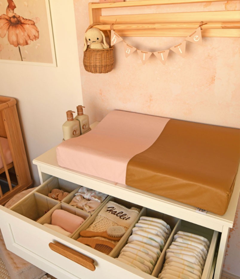 Changing pad for newborn placed on top of a wooden baby changing station filled with nappies and baby essentials for easy diaper changes.