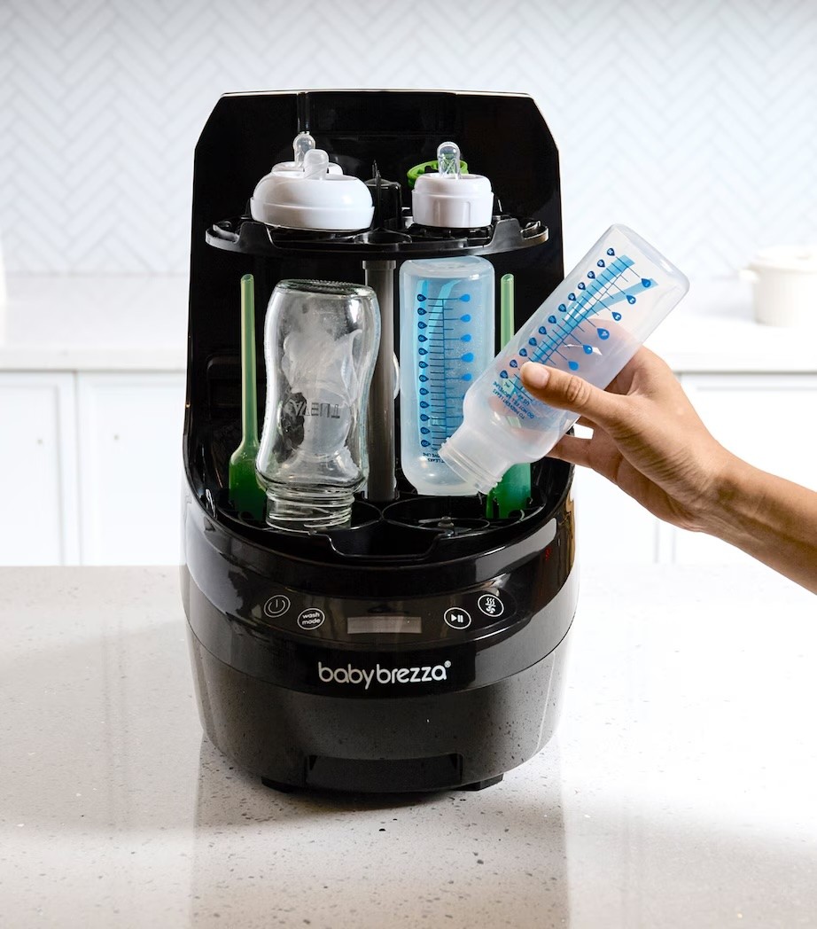 The Baby Brezza Bottle Washer Pro in black, shown with someone stacking baby bottles inside