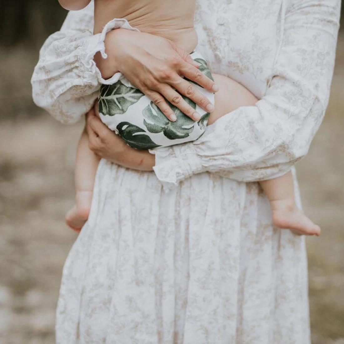 Mum holding baby wearing the best cloth nappies with a modern leafy design.
