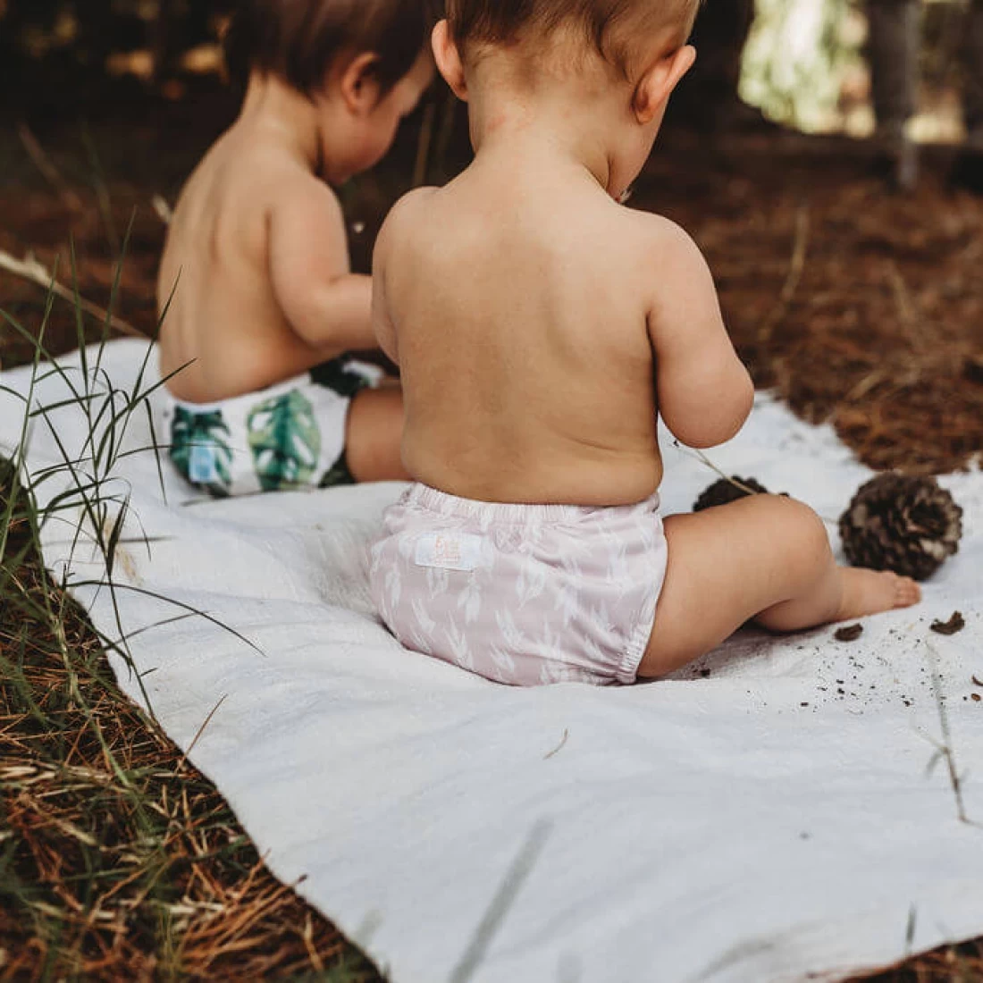Two babies sitting outdoors wearing the best cloth nappies in cute prints.