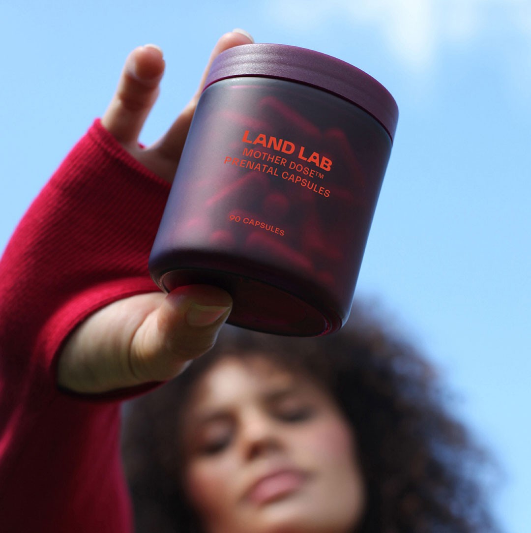 A pregnant woman holding a bottle of Mother Dose by Land Lab, one of the best prenatal vitamins in Australia