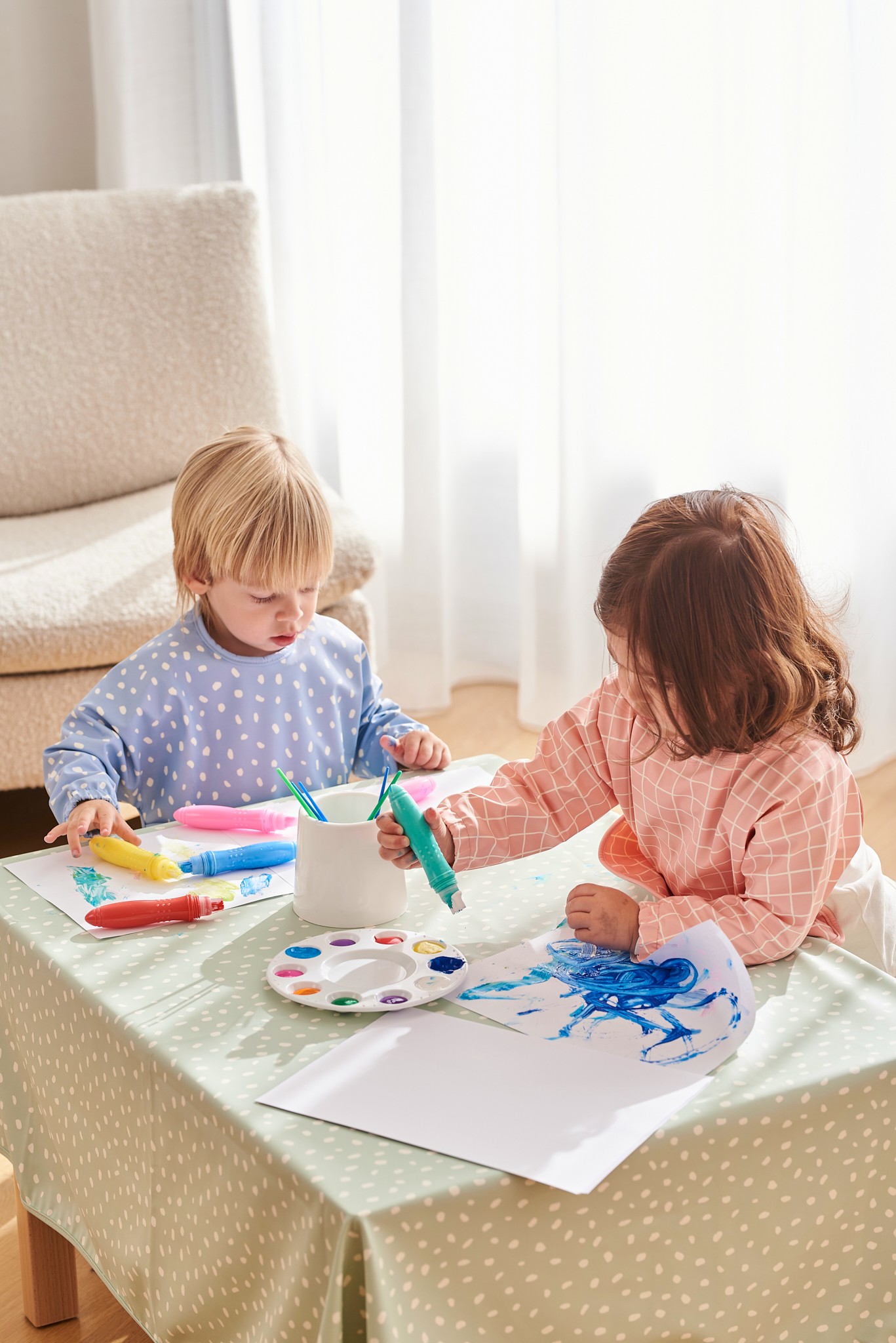 2 babies engaging in a fun drawing activity, both wearing Jae and Bae Sleeve Bibs, the Best Essential for keeping clothes clean.