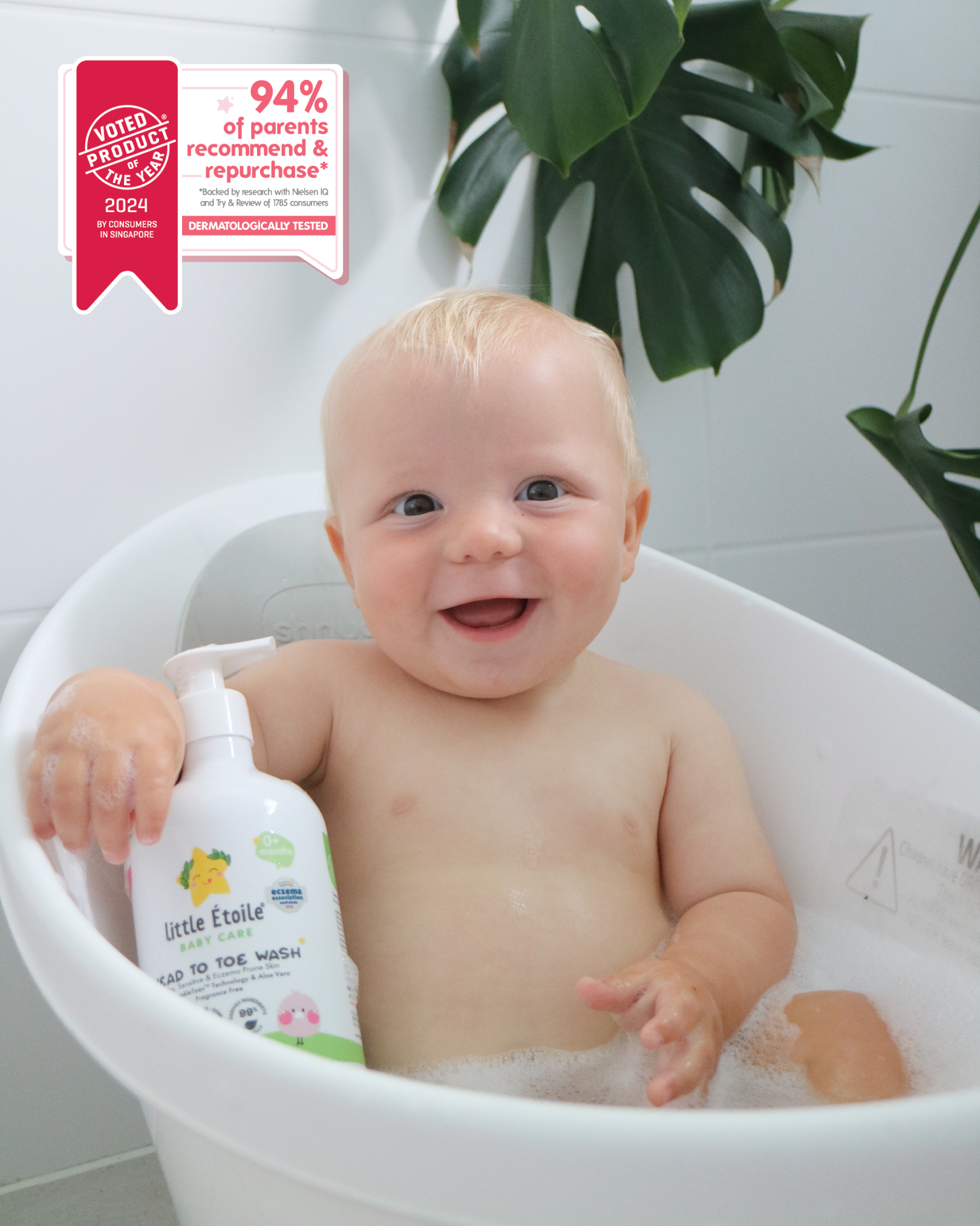 A baby is in the bathtub, holding a Little Étoile Baby Care product.