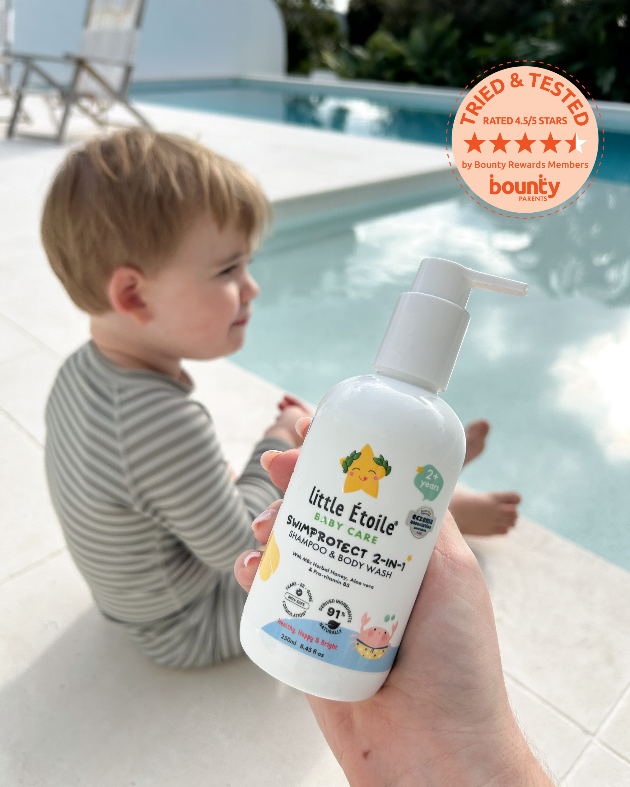 A toddler sits in a pool in the background while a mum’s hand holds a Little Étoile Baby Care product in the foreground.