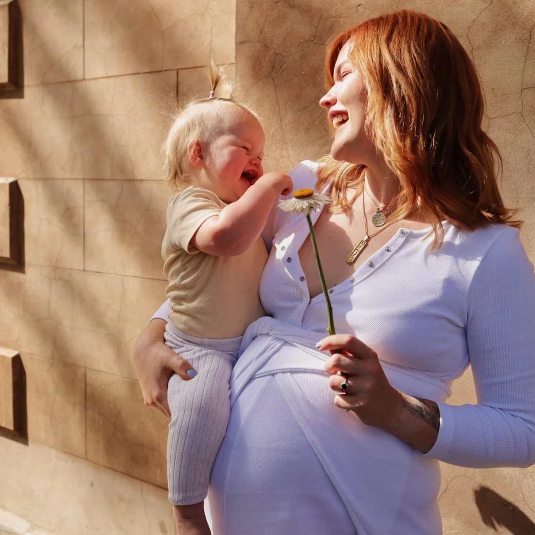Pregnant mum carrying her baby while wearing a purple Toots & Co maternity outfit, showcasing stylish and functional pregnancy fashion.